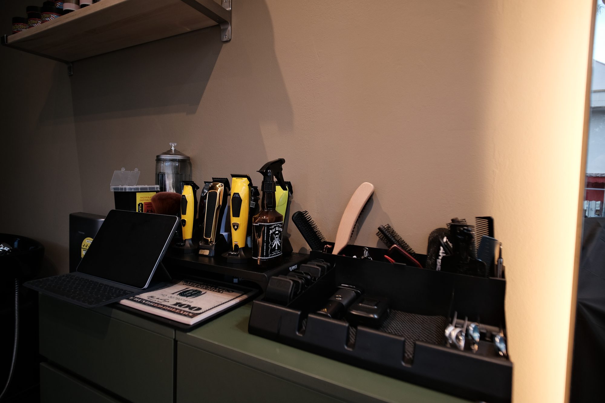 Barber tools and clippers on olive green cabinetry against warm clay walls